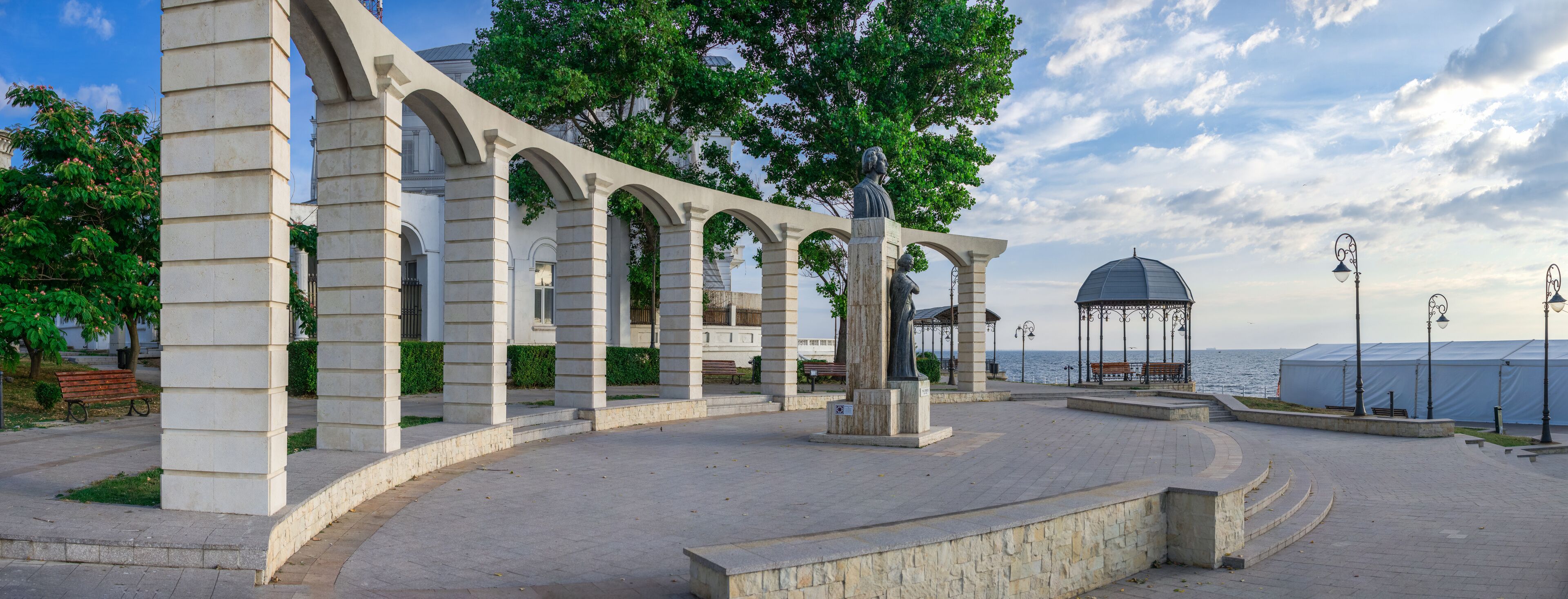 Un pabellón de piedra con arcos, una estatua y un mirador junto al mar.