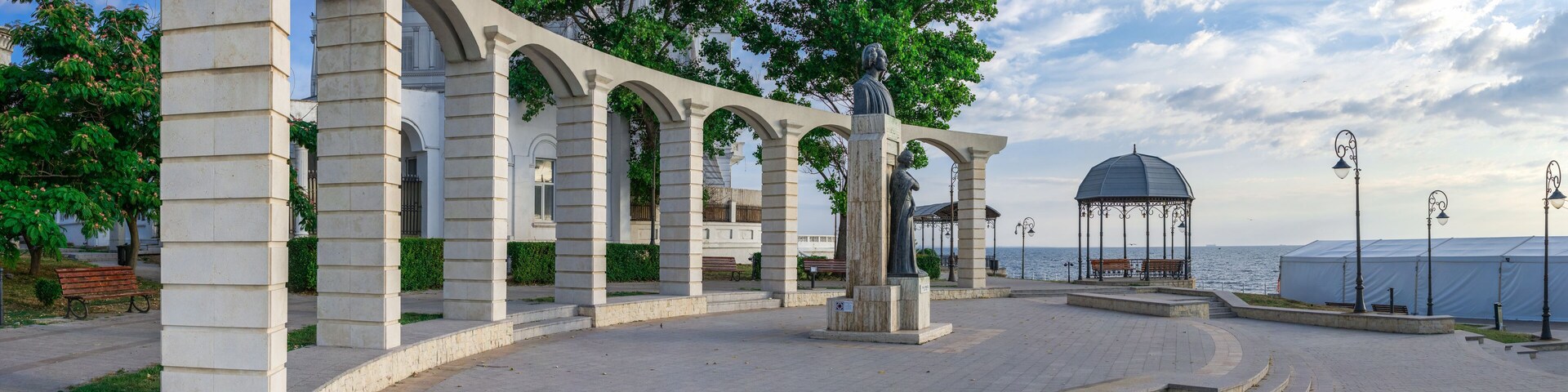Un pabellón de piedra con arcos, una estatua y un mirador junto al mar.