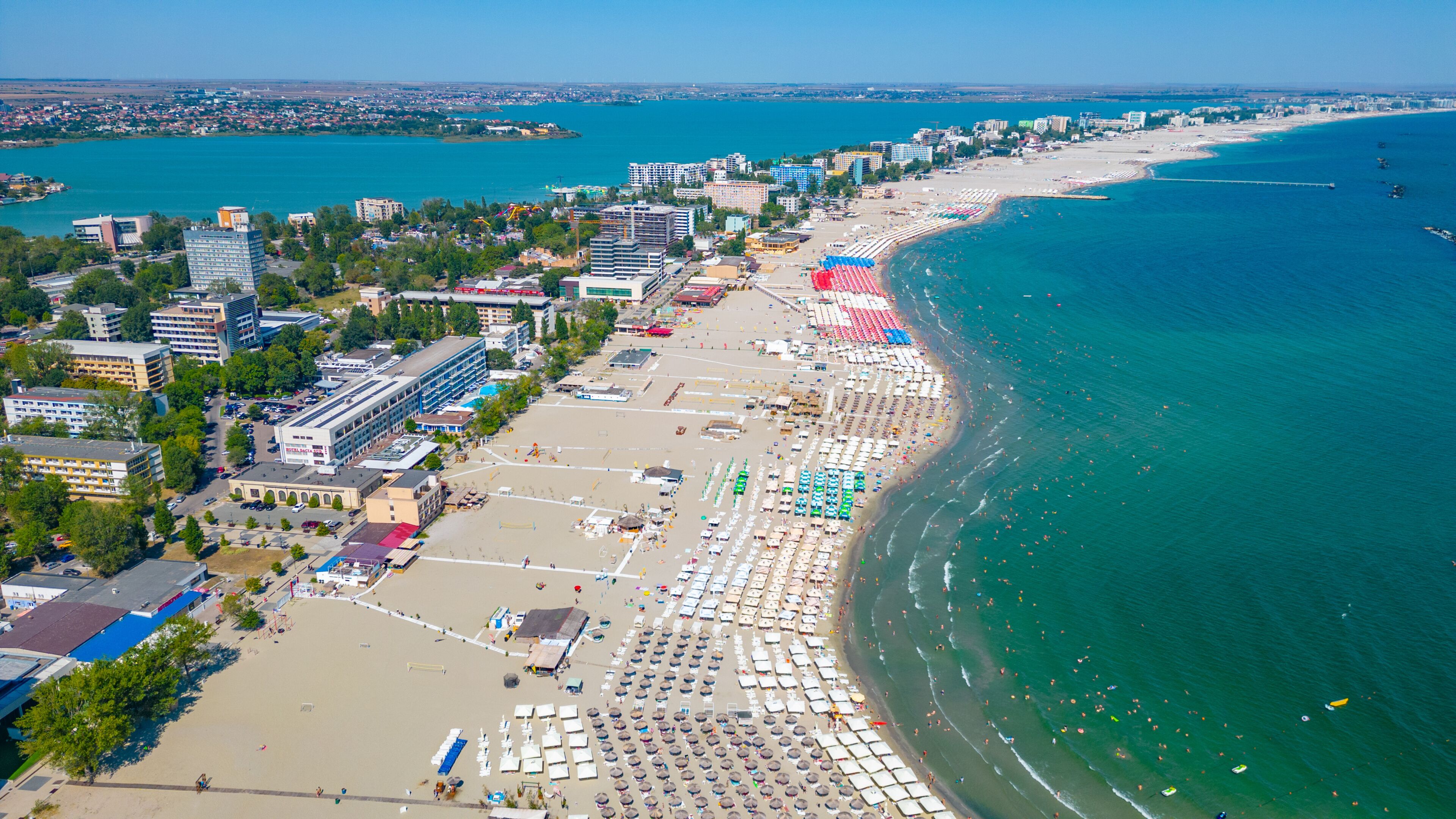 A coastal cityscape with a wide beach, clear blue waters, and dense urban buildings.
