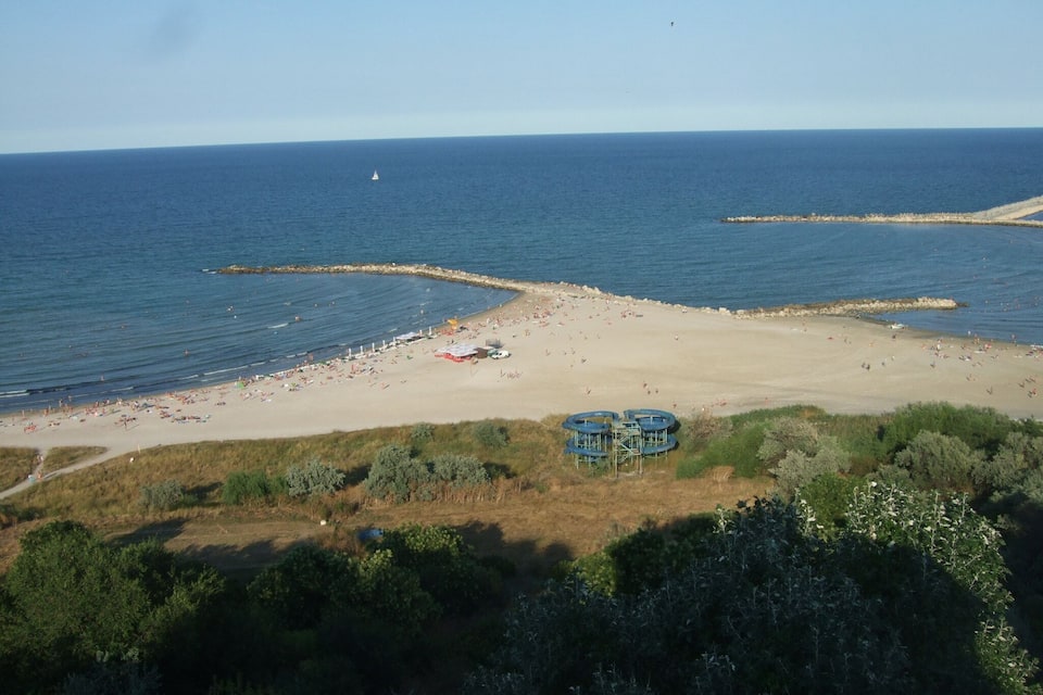 A beach with a rocky breakwater, sandy shore, and a small sailboat in the distance.