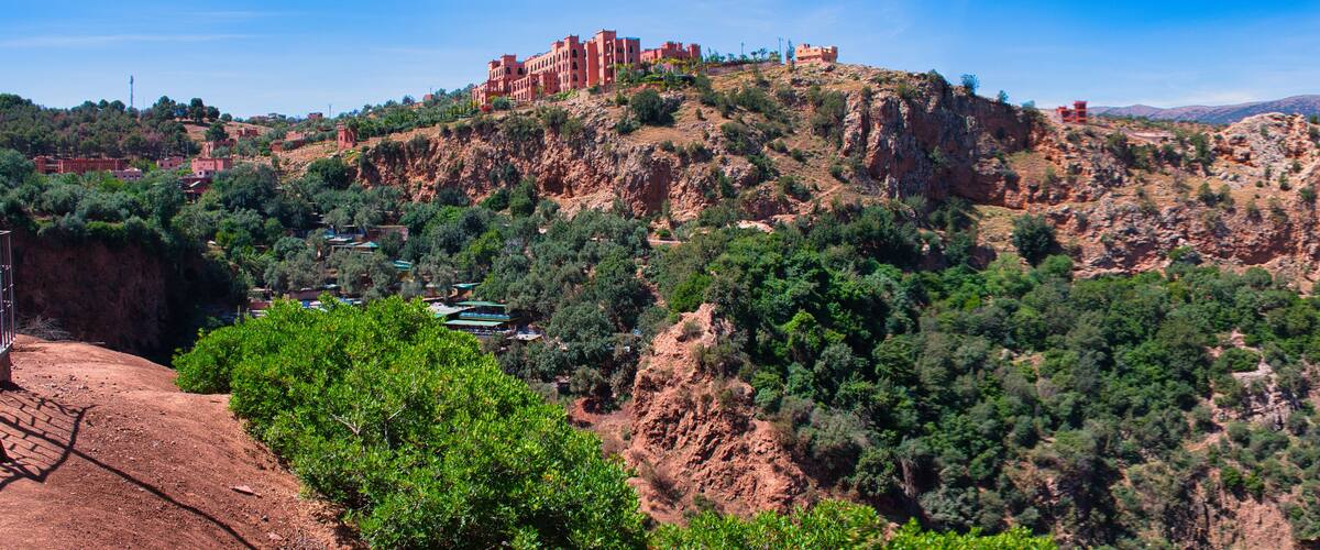 A mountainous landscape with a red-roofed building on top and a valley with greenery.
