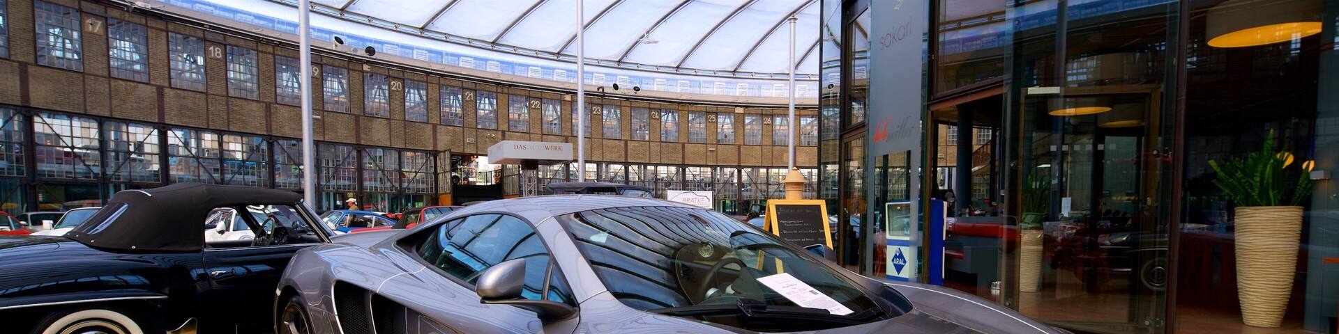 A silver sports car in a showroom with a large glass facade and a modern interior.