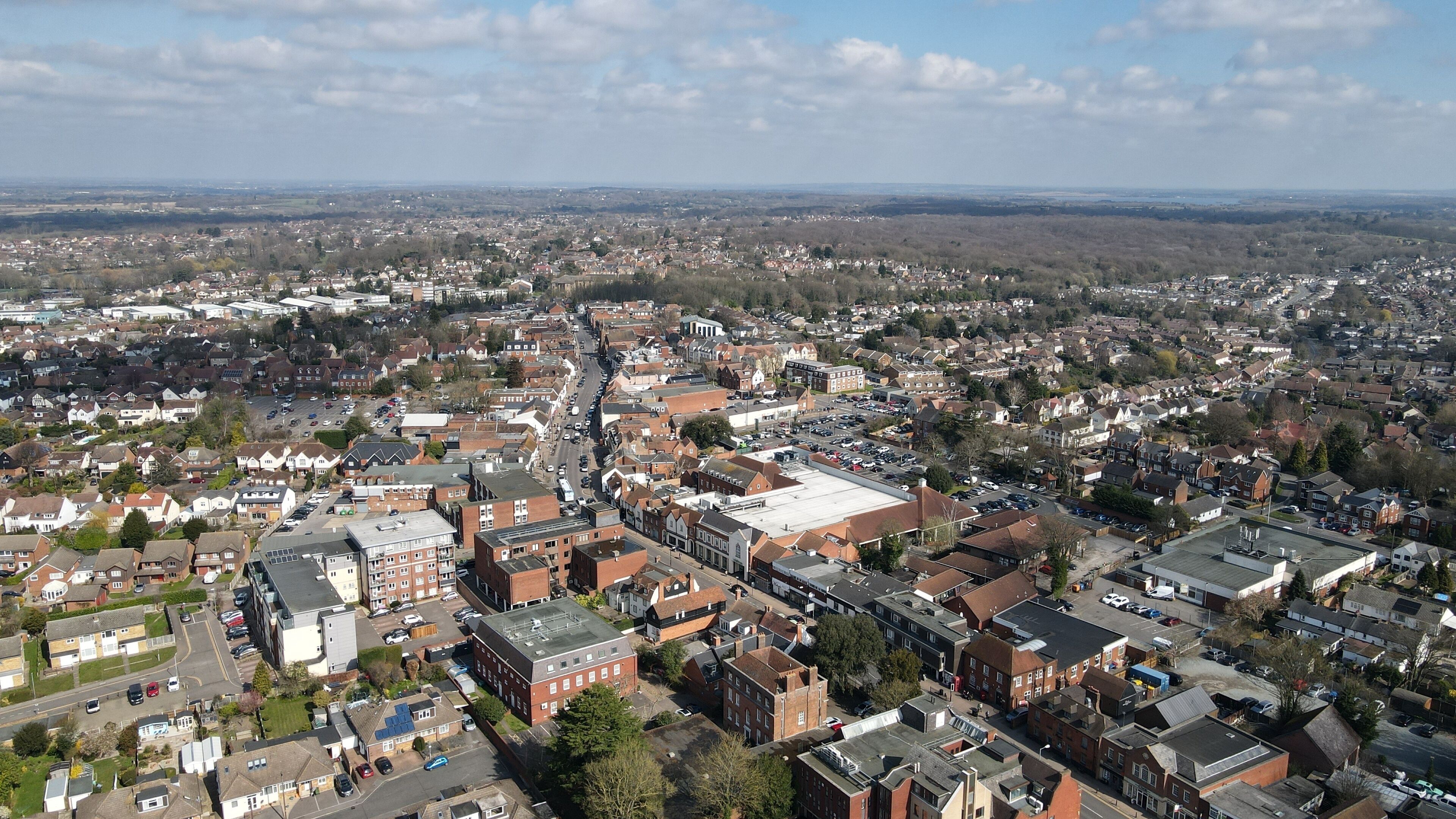 A densely populated urban area with a mix of residential and commercial buildings, a central road, and surrounding open fields.