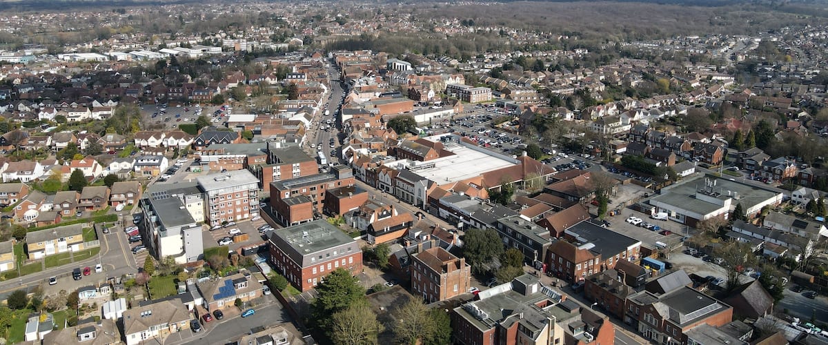 A densely populated urban area with a mix of residential and commercial buildings, a central road, and surrounding open fields.