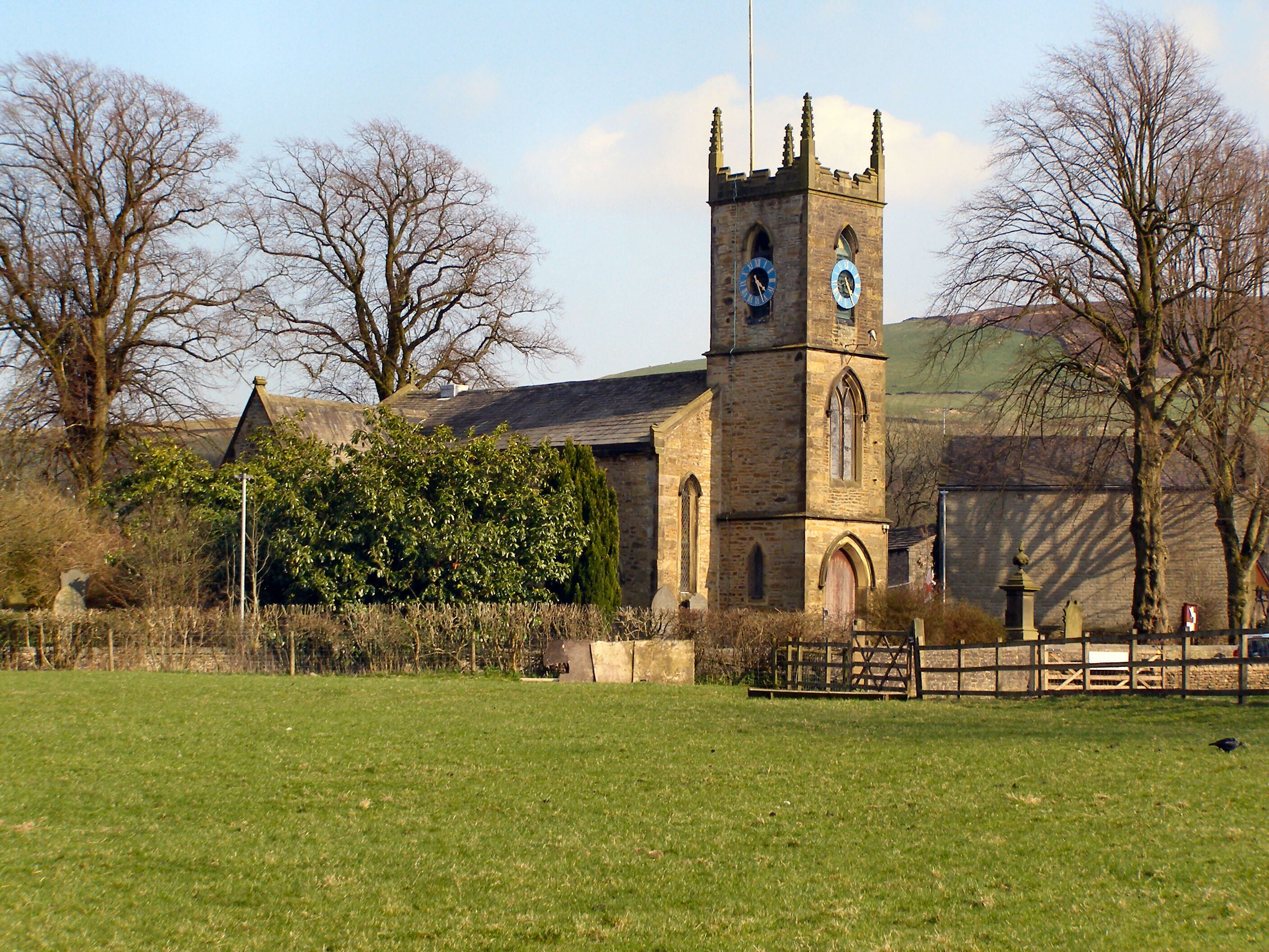 A church with a clock tower, surrounded by trees and a grassy field.