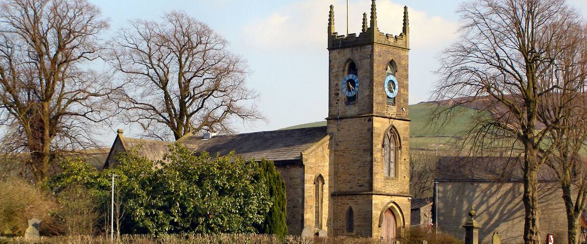 A church with a clock tower, surrounded by trees and a grassy field.