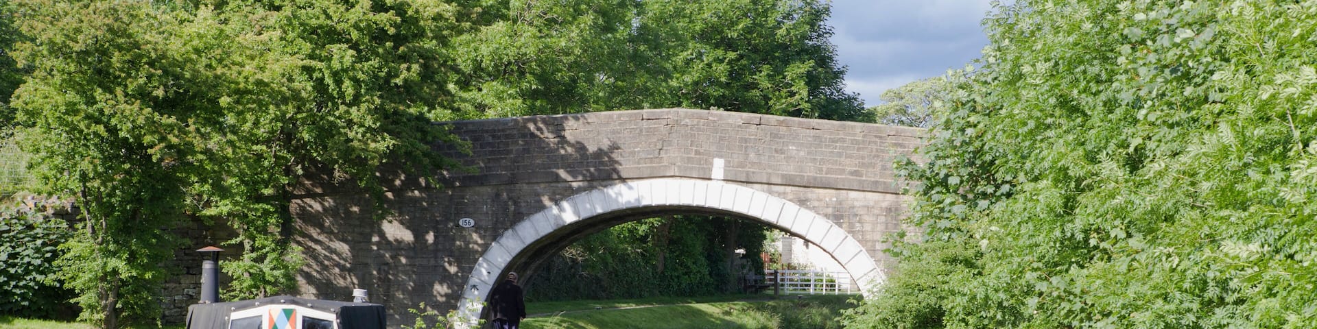 A quiet stretch of the Leeds and Liverpool Canal near Barnoldswick, with a single narrowboat moored alongside the tow-path, and an old canal bridge in the middle distance.