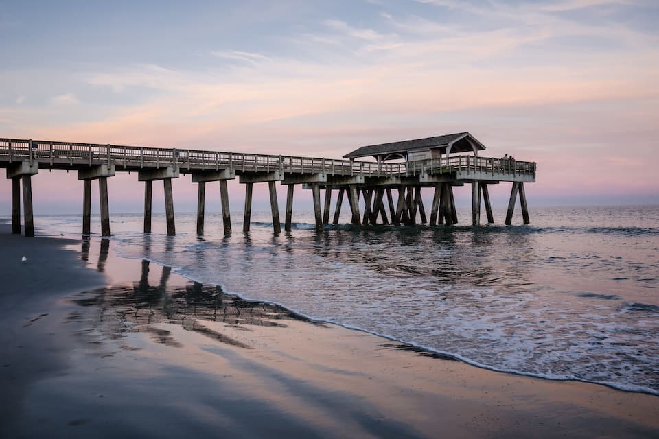 A pier extending into the water with a building on it, surrounded by calm sea and a clear sky.