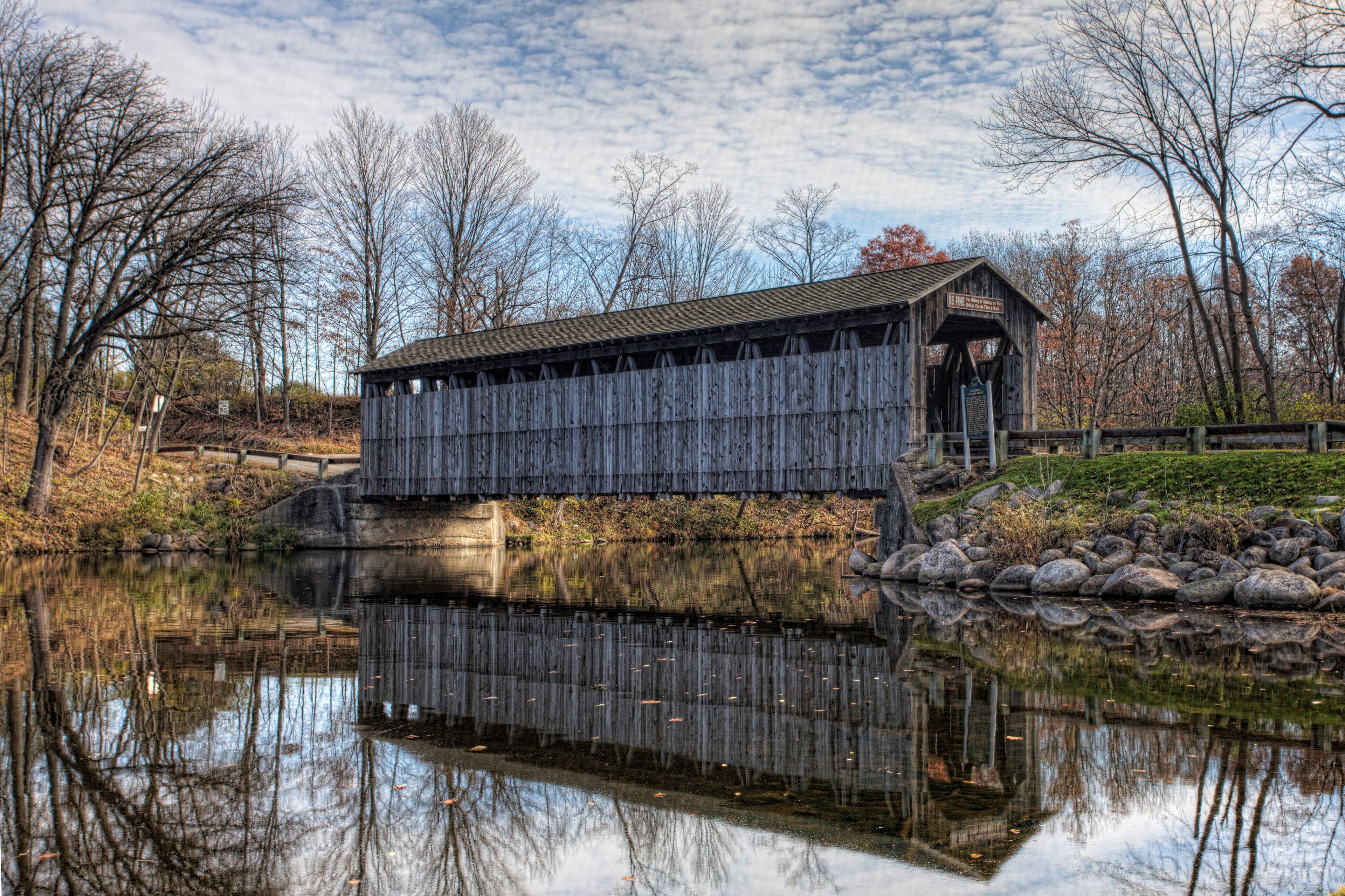 A wooden covered bridge over a calm river, surrounded by trees and rocks.