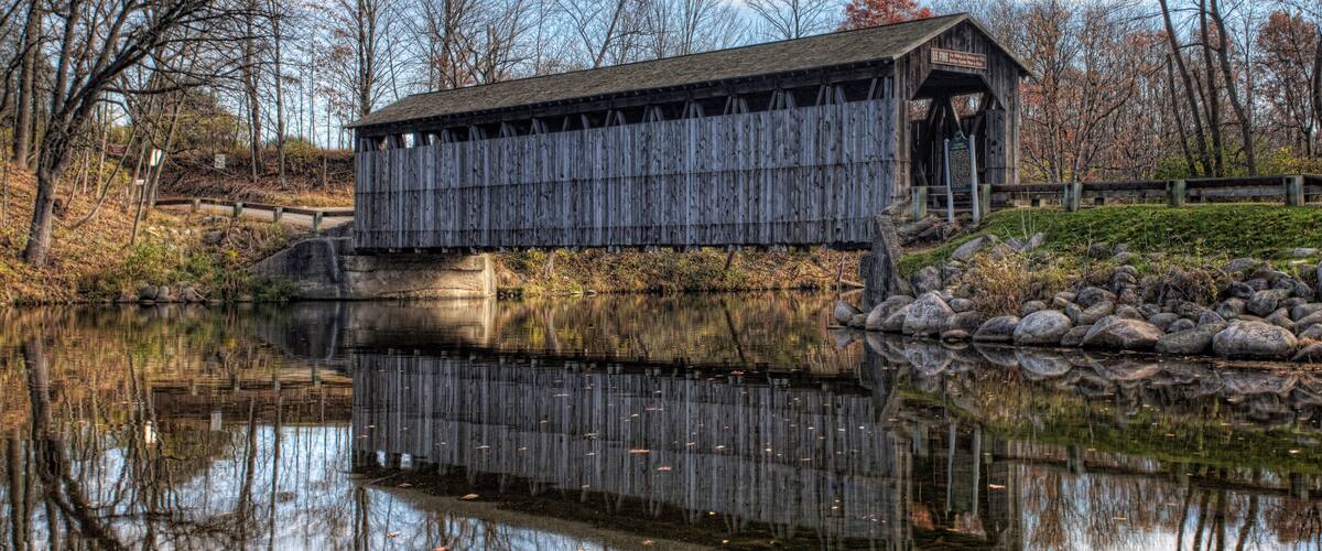A wooden covered bridge over a calm river, surrounded by trees and rocks.