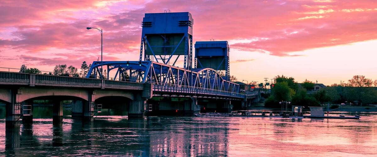 A bridge over a river with a sunset sky.