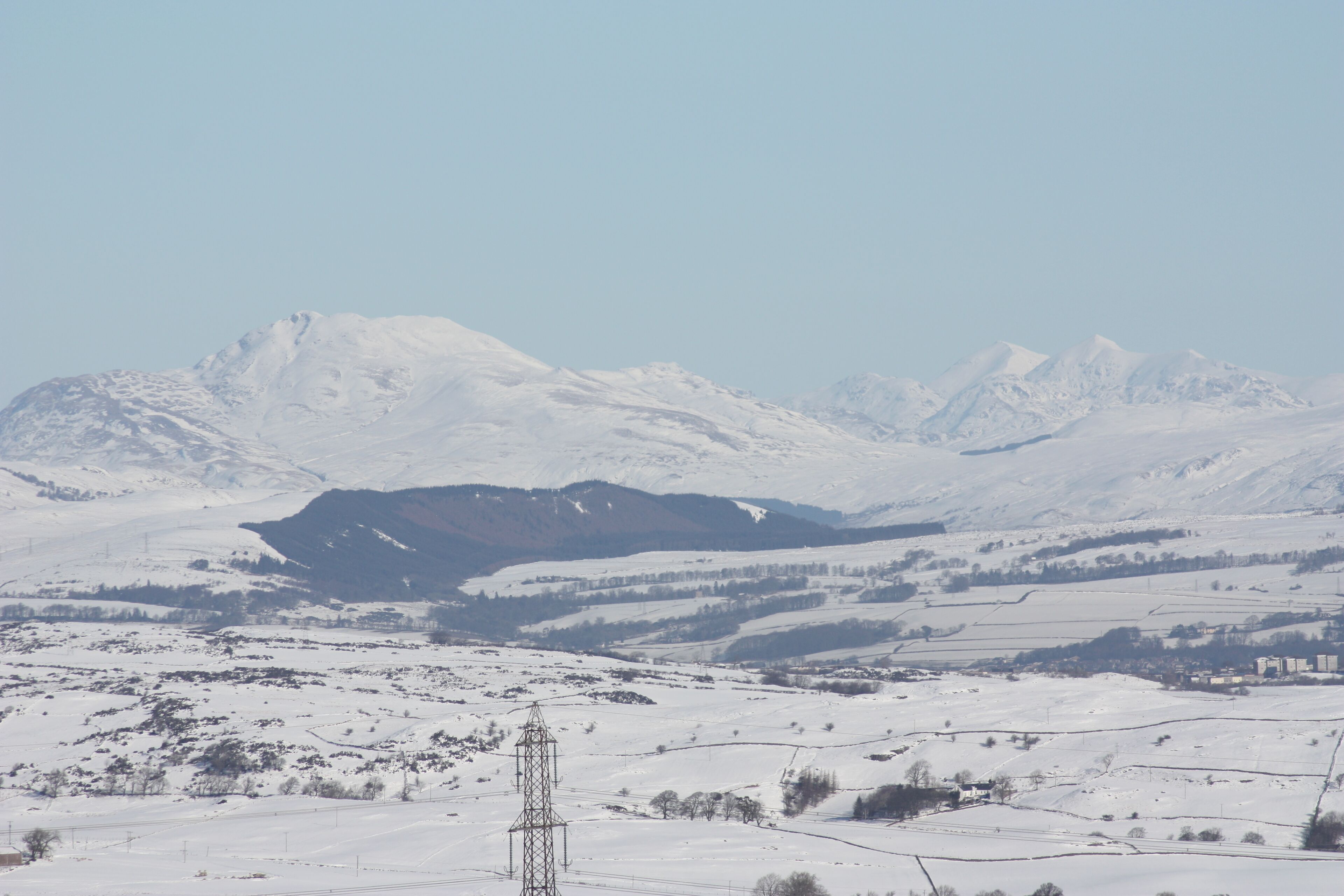 A snow-covered mountainous landscape with a power line tower in the foreground.