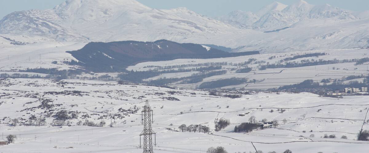 A snow-covered mountainous landscape with a power line tower in the foreground.