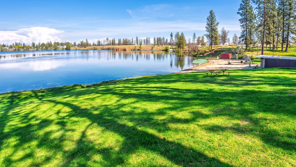 A lake with a grassy area, picnic tables, and a small shed.