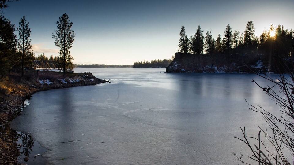 A frozen lake surrounded by trees and rocky terrain.