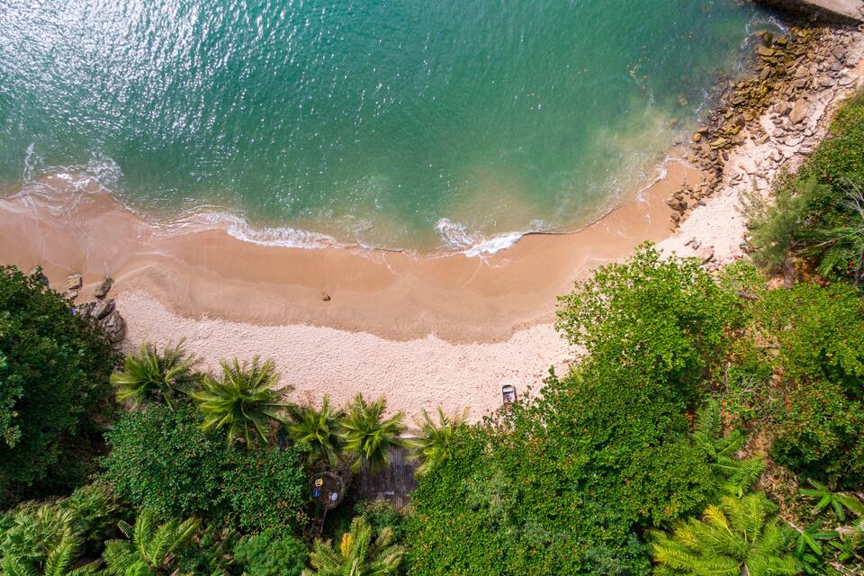 Vista aérea de una playa con agua turquesa cristalina, orilla arenosa y densa vegetación tropical.