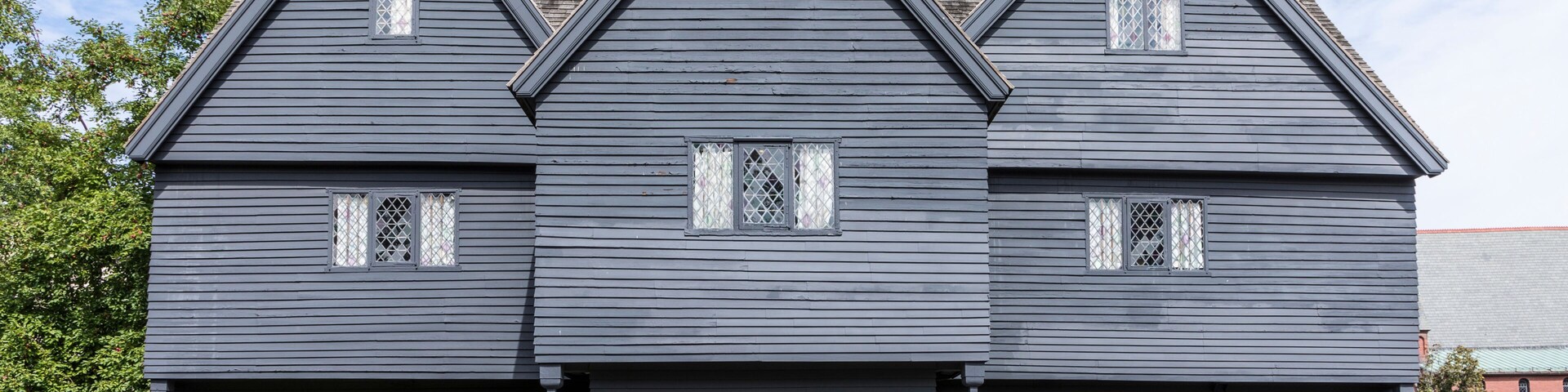 Una casa de dos pisos con fachada azul oscuro, un porche delantero y una guirnalda decorativa en la puerta.