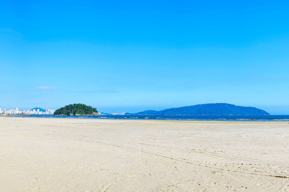 A wide sandy beach with a city skyline in the background and a mountain in the distance.