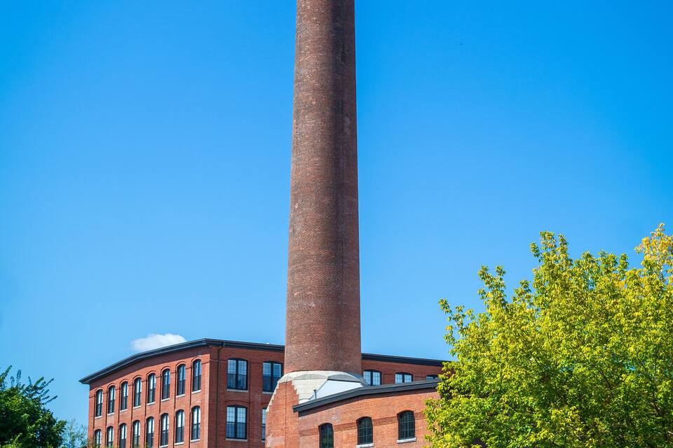 A tall brick chimney, a red brick building, and green trees.