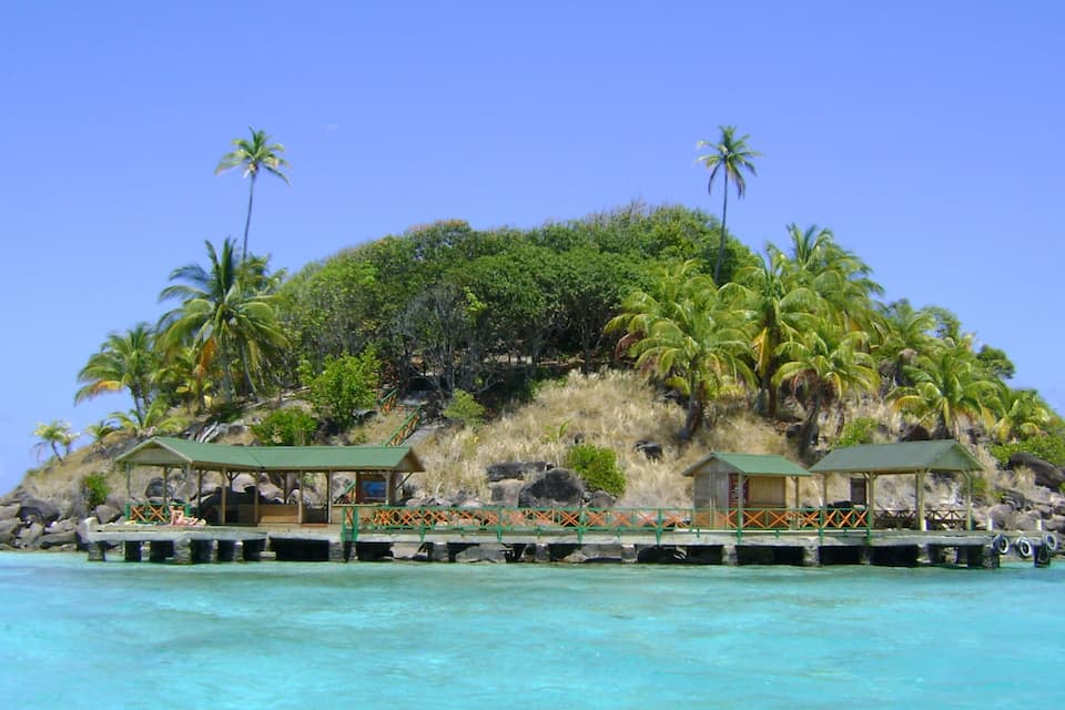 A tropical island with palm trees, a beach, and a pier with small buildings.