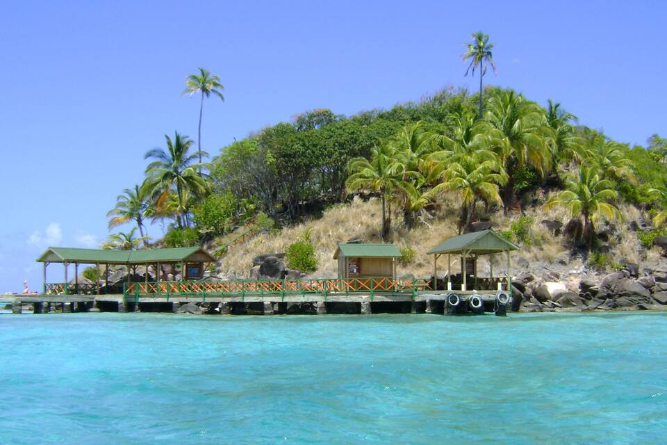 A tropical island with a wooden pier extending into turquoise waters, surrounded by lush greenery and palm trees.