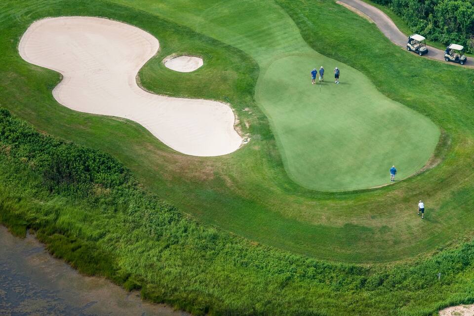 An aerial view of a golf course with sand bunkers, a water body, and players.