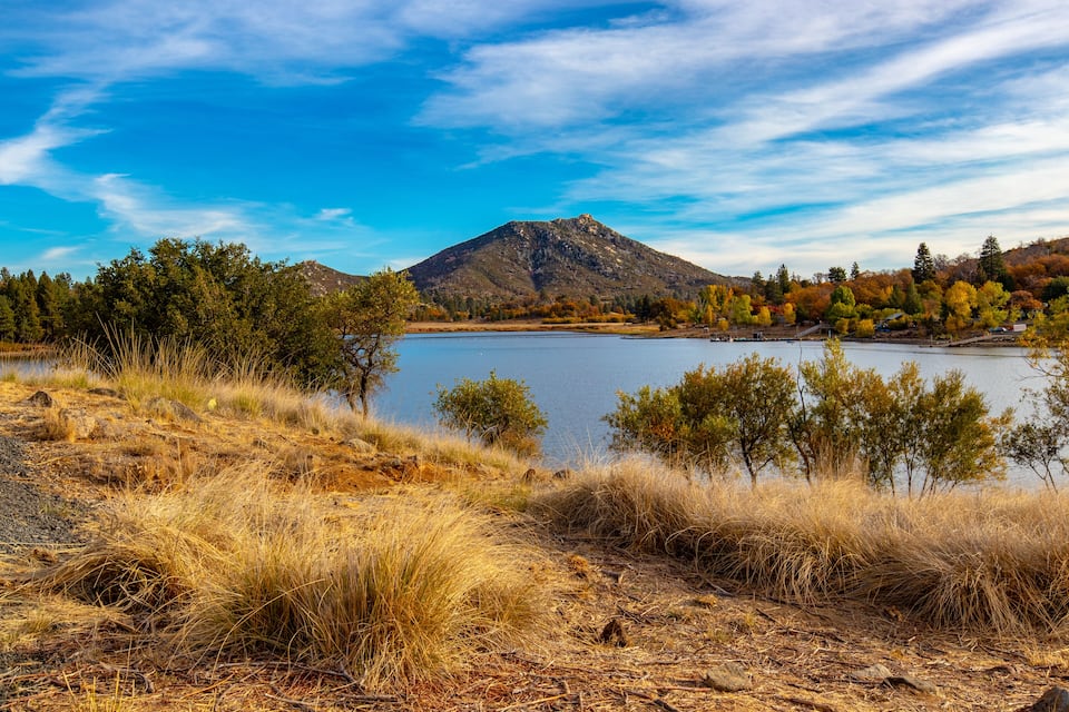 A lake surrounded by dry grass, trees, and a mountain.