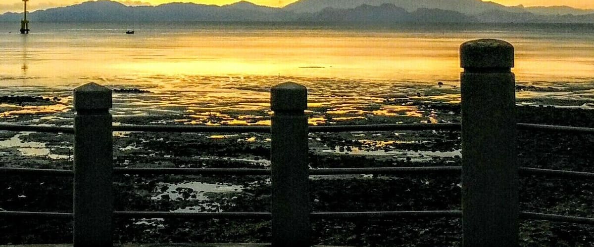 A sunset over a calm body of water with mountains in the background and a concrete barrier in the foreground.