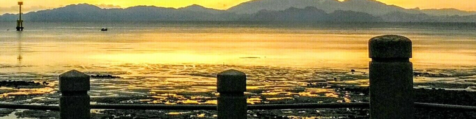 A sunset over a calm body of water with mountains in the background and a concrete barrier in the foreground.