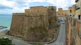 A stone fortification overlooking a coastal road with parked cars and a stop sign.