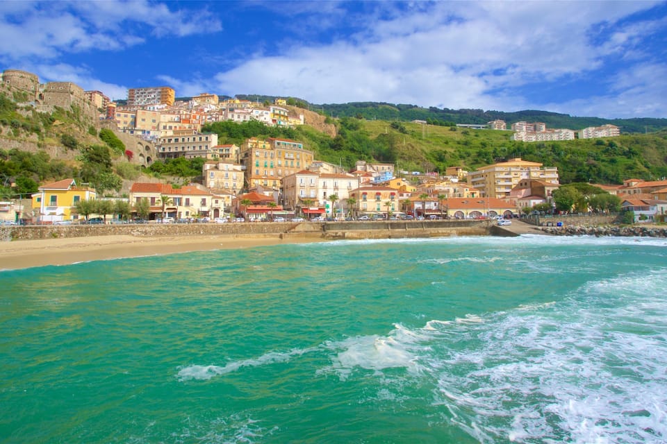 A coastal town with buildings on a hillside, a beach, and turquoise waters.