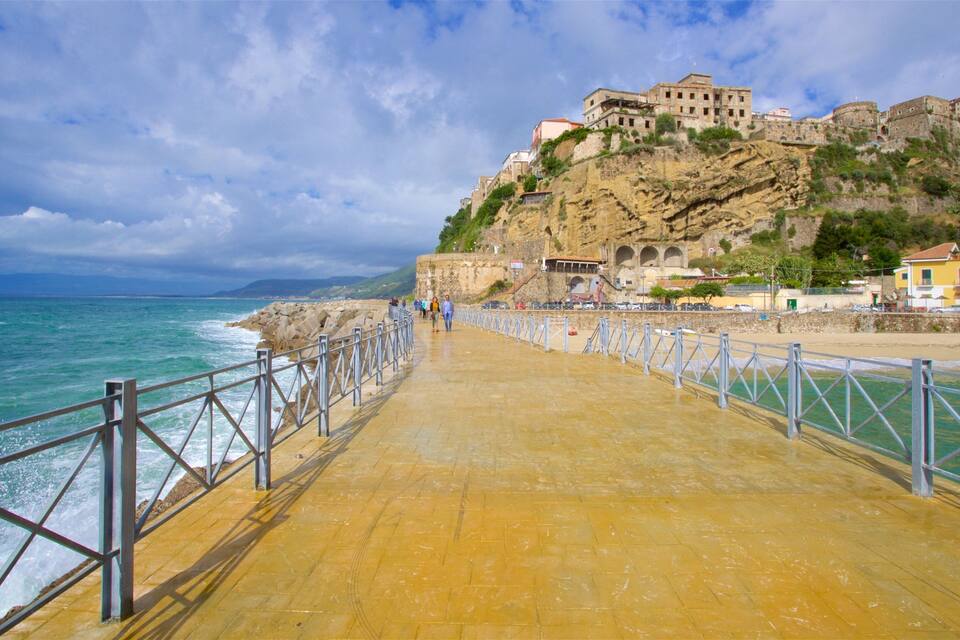 A coastal walkway with a historic building on a cliff, overlooking the sea.
