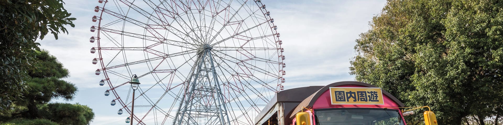 A pink train with a smiling face, a Ferris wheel, and a park with trees and bushes.