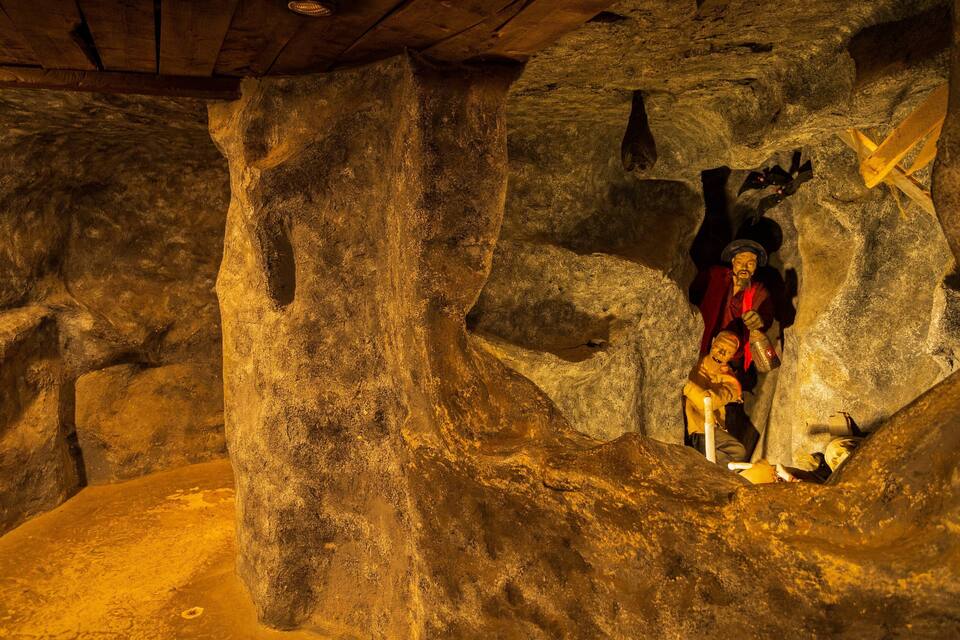 A cave with rock formations and a statue of a man holding a cross.