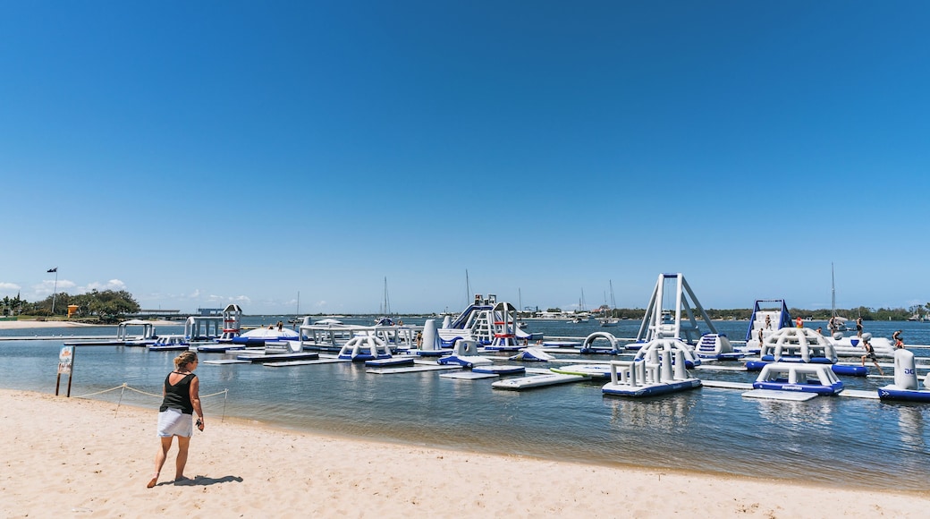 A beach with a clear sky, a woman standing on the sand, and several blue and white watercraft docked in the water.