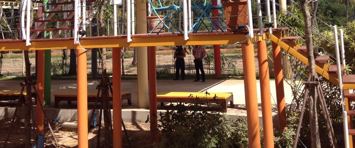 A colorful playground structure with a geometric design, surrounded by palm trees and a clear blue sky.