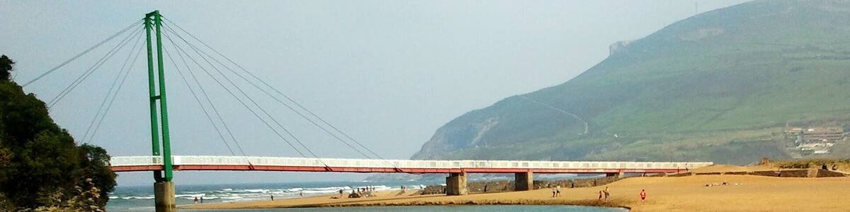 Eine Brücke über einem Fluss, mit einem Strand und Bergen im Hintergrund.