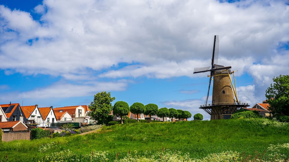 A windmill, houses, and a grassy hill.