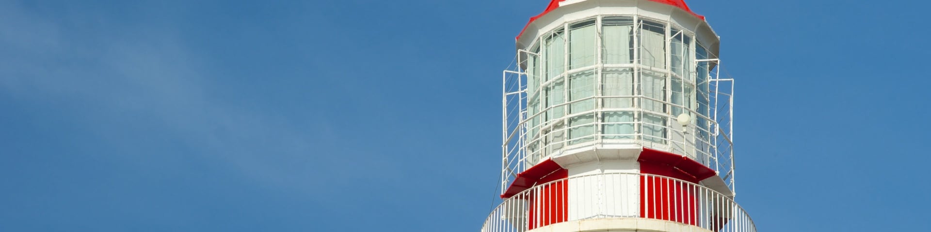 A lighthouse with a red top and white base against a clear blue sky.