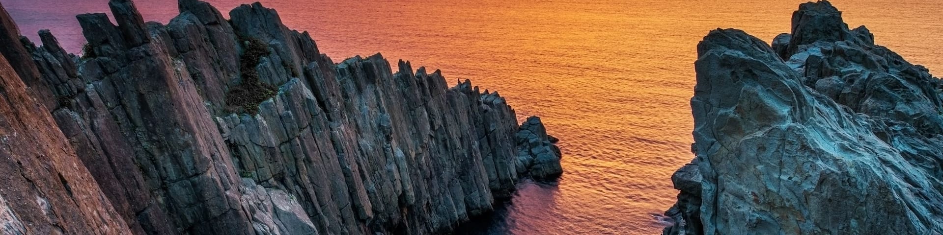 A coastal landscape with rocky cliffs and a narrow waterway during sunset.