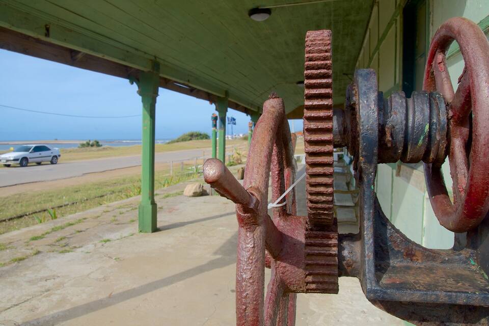 A coastal road with a green shelter, rusty gears, and a car in the distance.