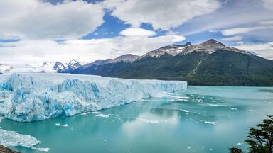 A glacier in a turquoise lake surrounded by mountains.
