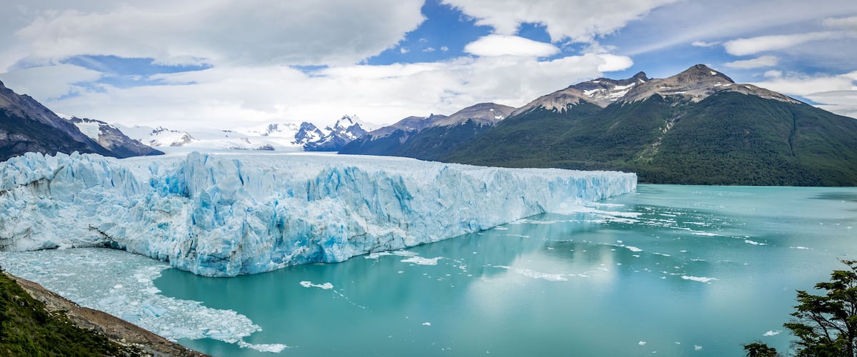 A glacier in a turquoise lake surrounded by mountains.