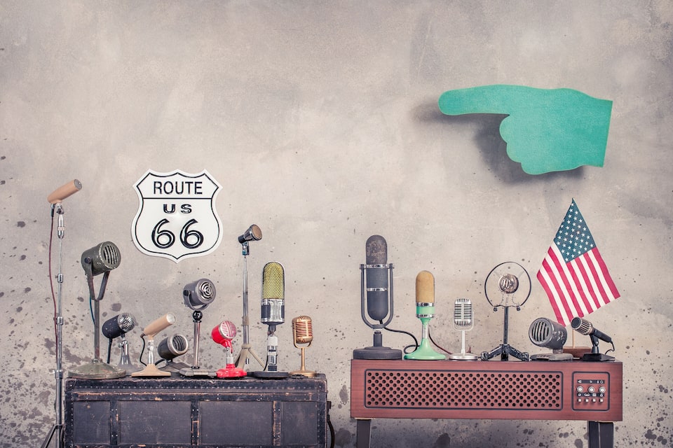 Retro microfoons, een Route 66 bord en een Amerikaanse vlag op een tafel voor een structuurwand.