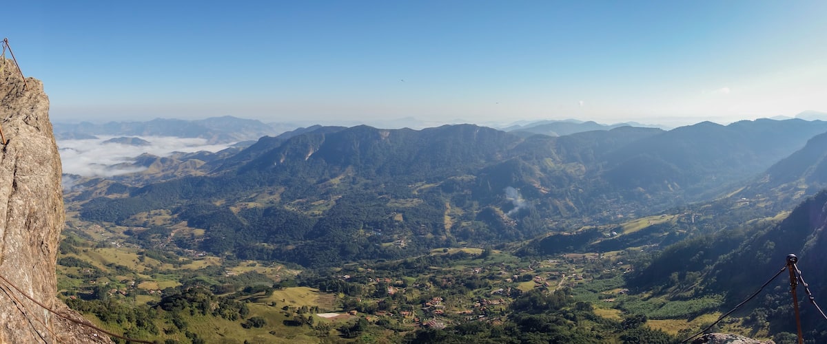 A mountainous landscape with a clear sky, a rocky outcrop on the left, and a village in the valley below.