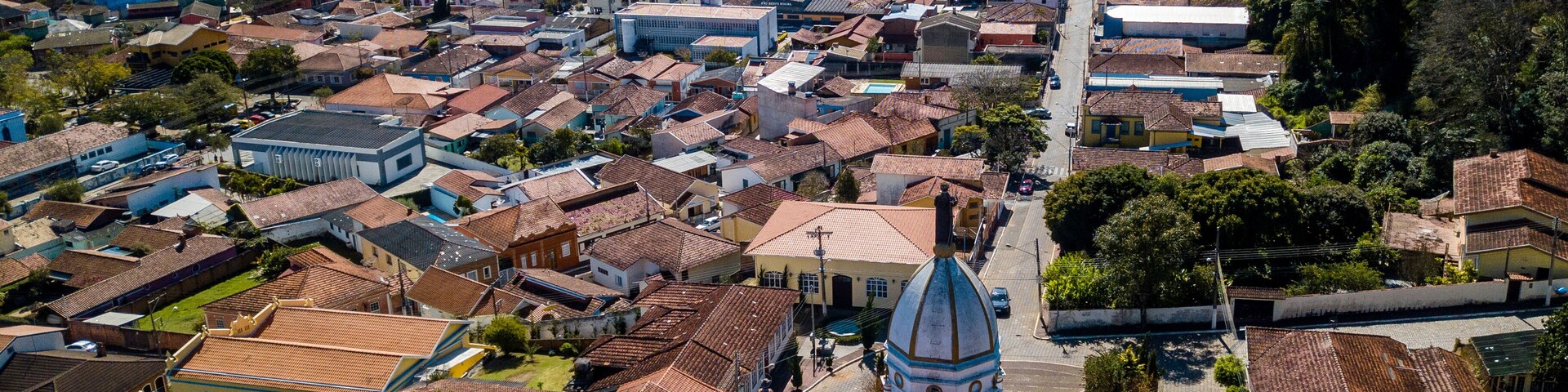 Vista aérea de un pueblo con una iglesia destacada, edificios con tejados de tejas rojas y zonas verdes circundantes.