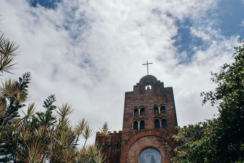 Een bakstenen kerk met een kruis bovenop, omringd door palmbomen.