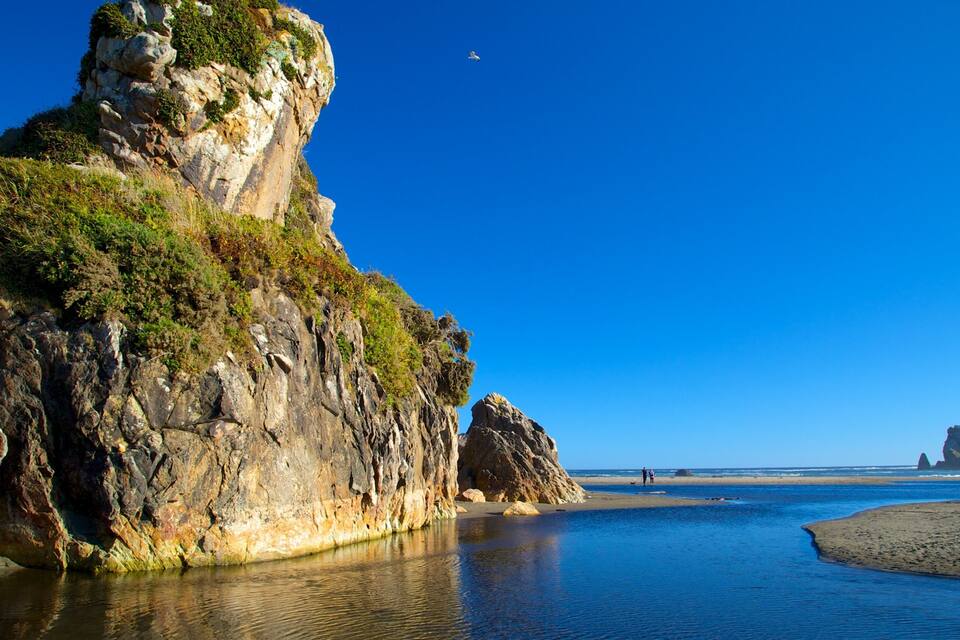 A coastal landscape with rocky cliffs, calm waters, and a clear blue sky.