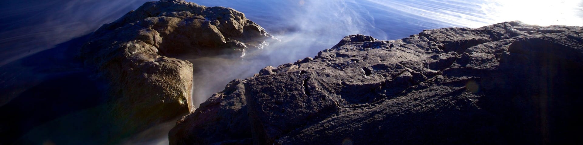 Une côte rocheuse, enveloppée de brume au-dessus de l’eau, avec des collines qui se dessinent à l’horizon.