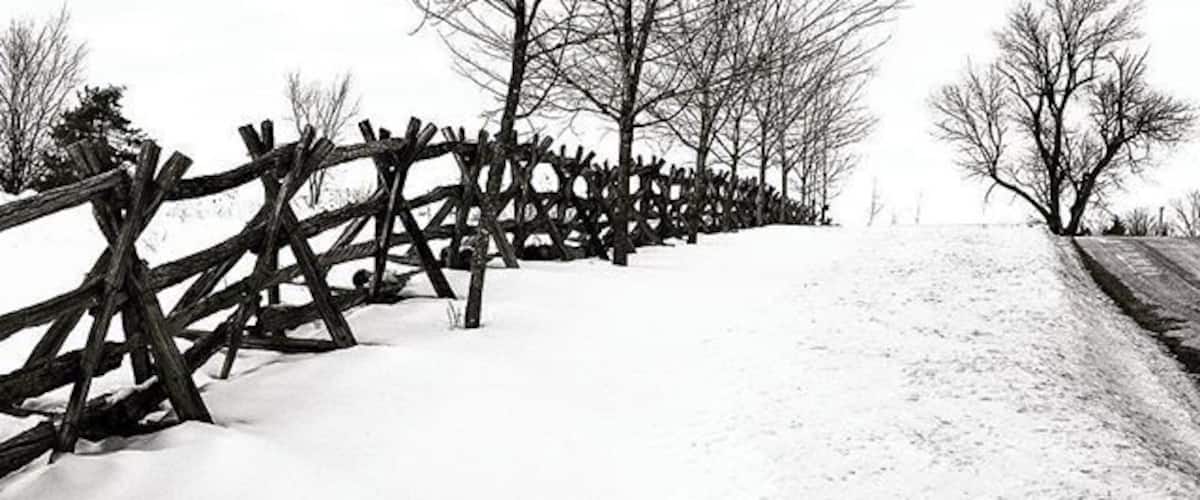 A snow-covered path with a wooden fence and leafless trees.